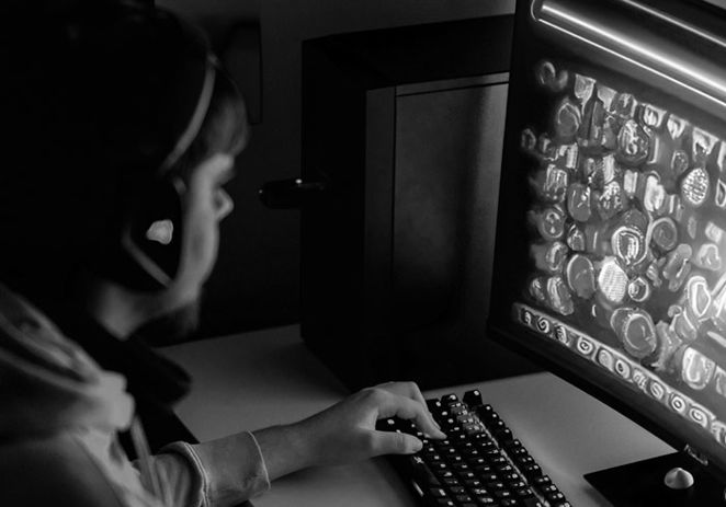 Ung kille som spelar på en dator, bara skärmen lyser i ett mörkt rum.