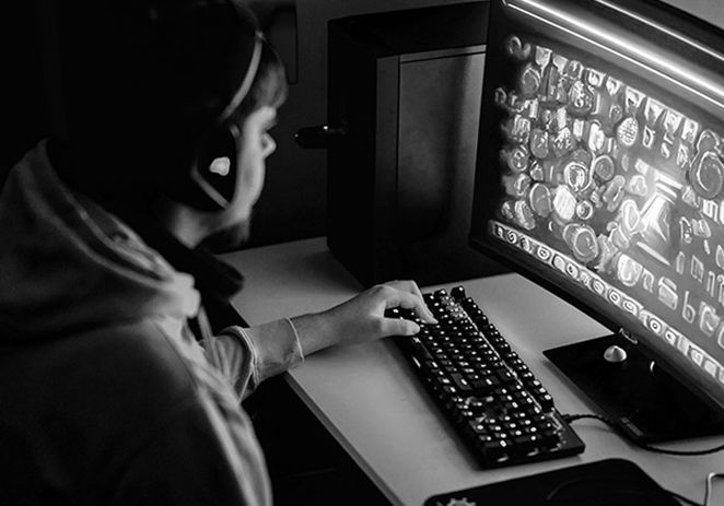 Ung kille som spelar på en dator, bara skärmen lyser i ett mörkt rum.